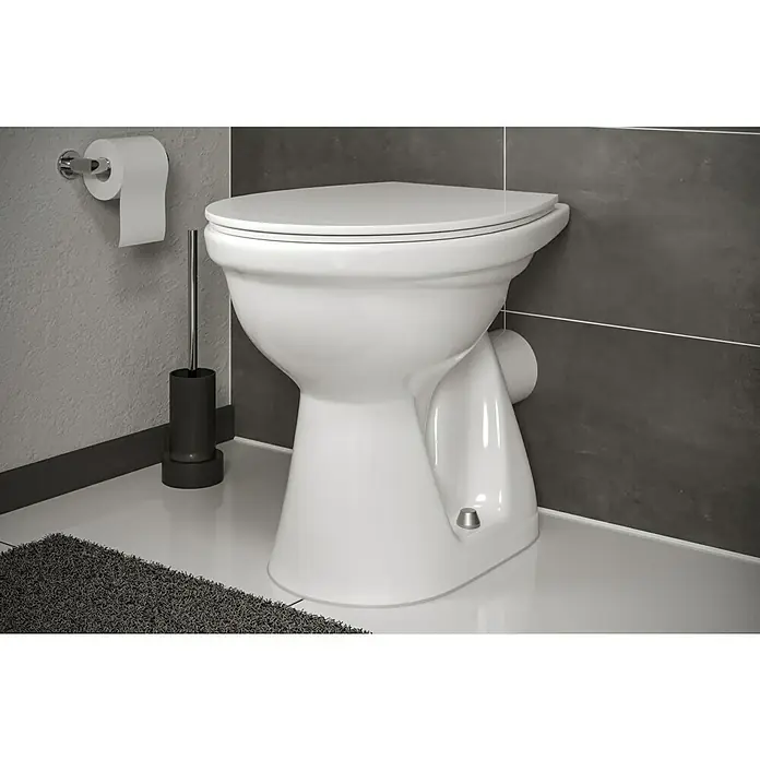 Simena Stand-WC - Mit Spülrand, Ohne Spezialglasur, Spülform: Tief, WC Abgang: Waagerecht, Weiß - Elegante Nahaufnahme einer weißen Toilette mit Toilettenpapierhalter und Bürste in einem modern gestalteten Badezimmer.