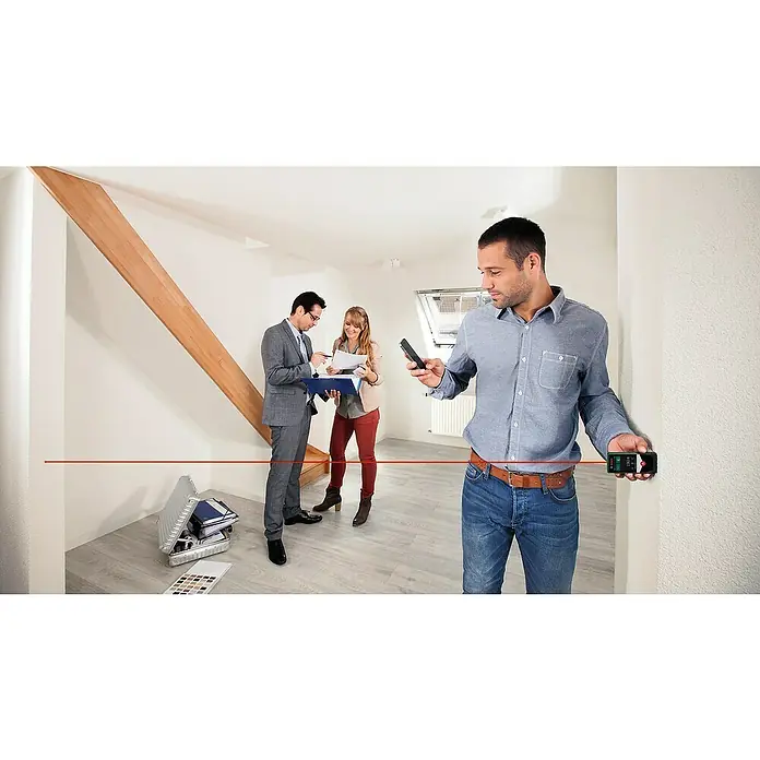 Bosch Advanced Laserentfernungsmesser AdvancedDistance 50 C - Messbereich: 0,05 - 50 m, Bluetooth 4.0 - Ein Mann benutzt ein digitales Laser-Entfernungsmessgerät in einem Raum, während andere im Hintergrund stehen.