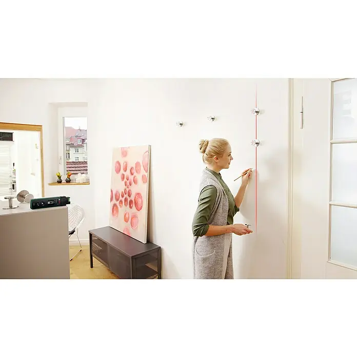 Bosch Linien-Adapter ZamoPassend für: Laser-Entfernungsmesser ZAMO IV - Eine Frau benutzt einen Bosch Kreuzlinienlaser, um eine gerade Linie an einer Wand zu markieren. Das Gerät steht auf einer Anrichte.