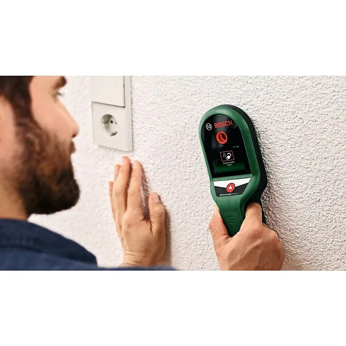 Bosch Ortungsgerät UniversalDetect - Geeignet für: Aufspüren von spannungsführenden Leitungen, Holz und Metall, Erfassungstiefe: Max. 50 mm stromführende Leitung - Ein Mann benutzt den Bosch UniversalDetect zur Ortung von Stromkabeln in der Wand. Das Gerät zeigt eine Warnung an.