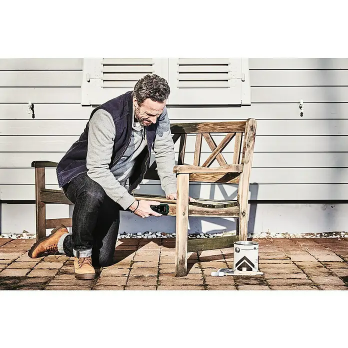 Bosch Universal Feuchtigkeitsmessgerät UniversalHumid - Geeignet für: Holz, Messbereich: 7,1 - 74,7 % - Mann misst Holzbank mit Laser-Entfernungsmesser. Renovierungsprojekt mit Farbdose und Pinsel auf Pflastersteinen im Freien.