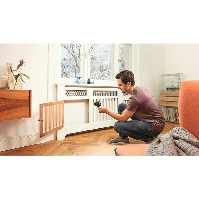 Bosch Universal Temperaturmessgerät UniversalTemp - Messbereich: -30 °C bis +500 °C - Mann hockt vor einem Heizkörper und benutzt einen Temperaturmesser, um die Temperatur der Heizung zu überprüfen.