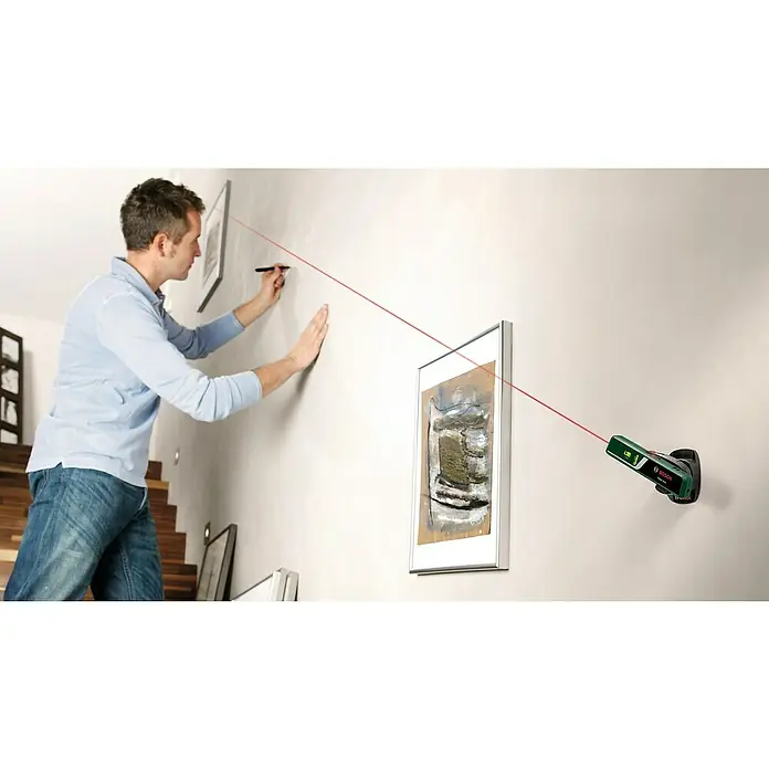 Bosch Easy Nivel láser Level - Número de niveles de burbuja: 2 ud. - Un hombre usa un medidor de distancia láser Bosch para alinear cuadros en la pared. La línea láser roja lo ayuda en esta tarea.