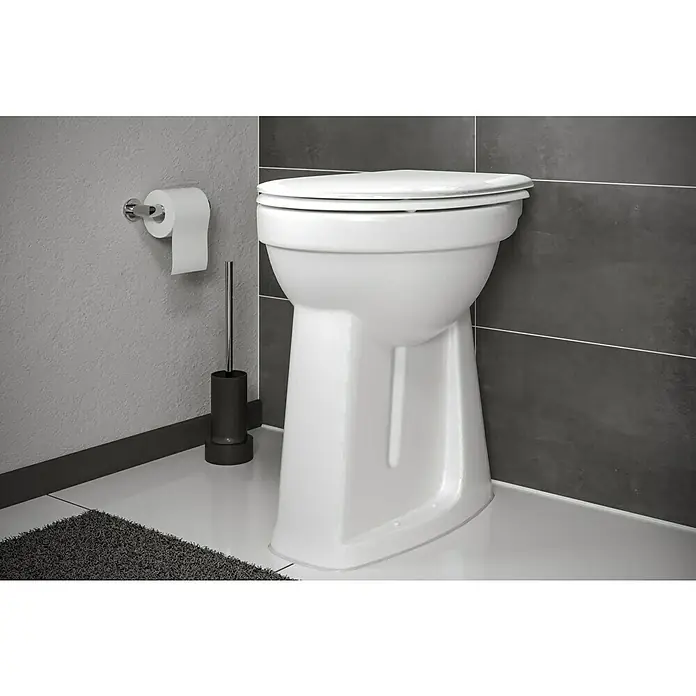 Camargue Stand-WC-Set Plus 100Mit Spülrand, Ohne Spezialglasur, Spülform: Flach, WC Abgang: Senkrecht, Weiß - Nahaufnahme einer weißen Toilette mit geschlossenem Deckel in einem Badezimmer mit grauen Fliesen und einem Toilettenpapierhalter.