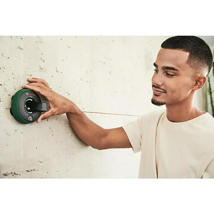 Bosch Linienlaser Atino - Max. Arbeitsbereich: 2 m - 2,2 m - Ein Mann befestigt mit einer Hand einen Bosch Quigo Green Linienlaser an einer Wand. Das Gerät projiziert eine rote Linie.