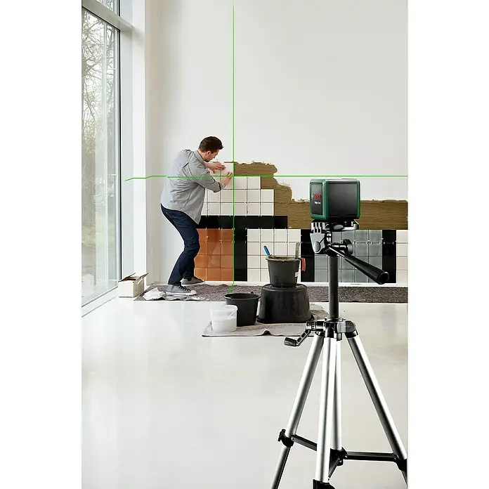 Bosch Kreuzlinienlaser Quigo Green - Max. Arbeitsbereich: 12 m - Fliesenleger verwendet einen Bosch Linienlaser auf einem Stativ für präzise Ausrichtung. Das grüne Laserlicht hilft bei der exakten Anbringung der Fliesen.
