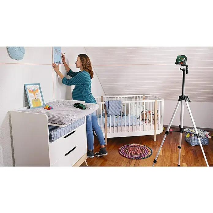 Bosch Kreuzlinienlaser UniversalLevel - Max. Arbeitsbereich: 10 m, 5 -tlg. - Eine schwangere Frau richtet mit dem Bosch Kreuzlinienlaser eine Bildergalerie in einem Kinderzimmer aus.