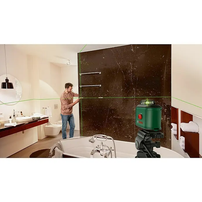 Bosch Kreuzlinienlaser UniversalLevel 360 - Max. Arbeitsbereich: 12 m, 6 -tlg. - Der Bosch Kreuzlinienlaser projiziert grüne Linien im Badezimmer, während ein Mann Handtuchhalter montiert.