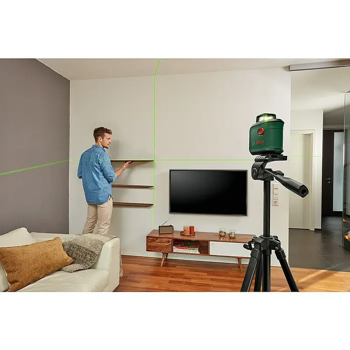 Bosch Kreuzlinienlaser AdvancedLevel 360Max. Arbeitsbereich: 12 m, 7 -tlg. - Ein Bosch Linienlaser projiziert grüne Laserlinien an die Wand, während ein Mann Regale montiert. Präzision beim Heimwerken!