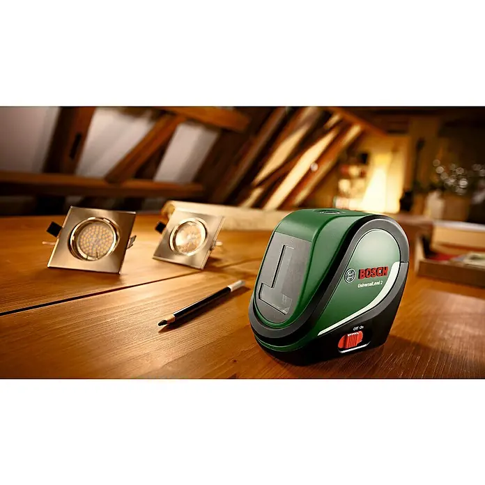 Bosch Kreuzlinienlaser UniversalLevel - Max. Arbeitsbereich: 10 m, 5 -tlg. - Das Bild zeigt den Bosch UniversalLevel 2 Kreuzlinienlaser, zwei quadratische LED-Einbaustrahler und einen Bleistift auf einer Holzoberfläche.