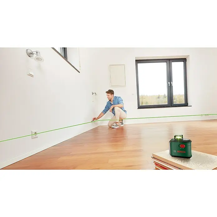 Bosch Kreuzlinienlaser AdvancedLevel 360Max. Arbeitsbereich: 12 m, 6 -tlg. - Ein Mann benutzt einen Bosch-Laser-Wasserwaage, um eine grüne Linie an der Wand zu markieren, während er auf dem Boden kniet.