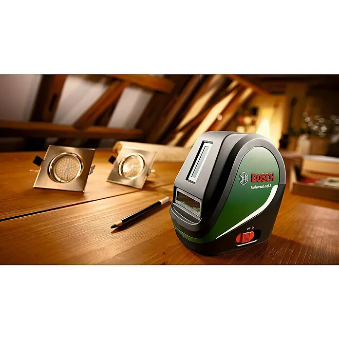 Bosch Kreuzlinienlaser UniversalLevel 3 - Max. Arbeitsbereich: 10 m, 5 -tlg. - Der Bosch UniversalLevel 3 Kreuzlinienlaser auf einem Tisch, neben zwei quadratischen LED-Leuchten und einem Bleistift.