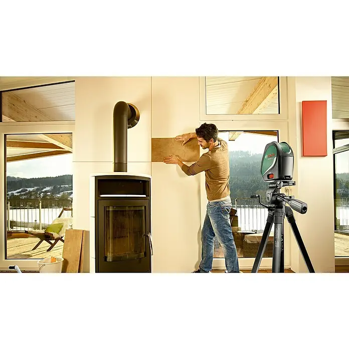 Bosch Stativ TT 150 - Höhenverstellung: 55 cm - 157 cm - Ein Mann verlegt Fliesen mit einem Bosch-Laser-Nivelliergerät, um die perfekte Ausrichtung zu gewährleisten, während er sein Wohnzimmer renoviert.