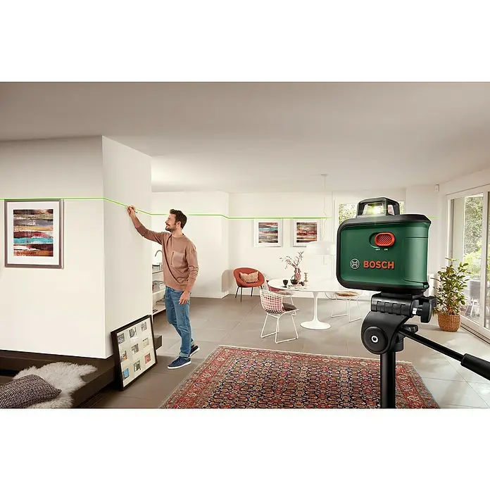 Bosch Stativ TT 150 - Höhenverstellung: 55 cm - 157 cm - Bosch Kreuzlinienlaser: Der grüne Laser projiziert präzise horizontale und vertikale Linien an die Wand, während ein Mann eine Markierung setzt.
