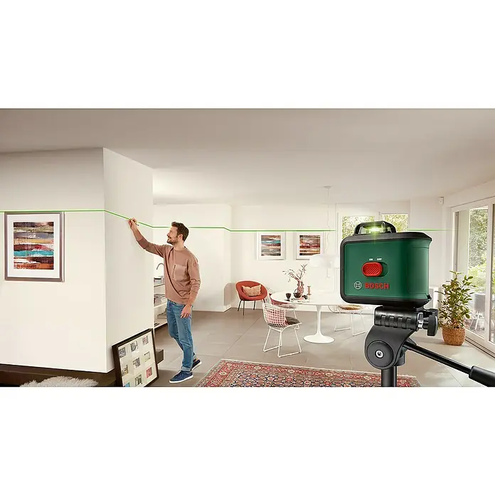 Bosch Kreuzlinienlaser UniversalLevel 360 - Max. Arbeitsbereich: 12 m, 6 -tlg. - Der Bosch Kreuzlinienlaser projiziert grüne Linien an Wände, während ein Mann Markierungen setzt. Praktisches Werkzeug für präzise Ausrichtung.