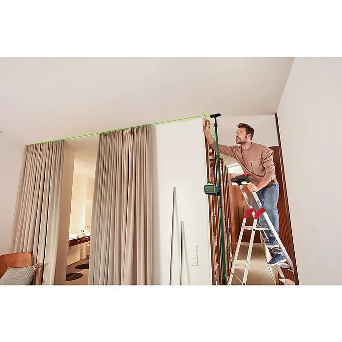Bosch Teleskopstange TP 320 - Kunststoff, Arbeitshöhe: 10 cm - 320 cm - Ein Mann auf einer Leiter verwendet ein Bosch-Lasergerät, um eine grüne Linie an der Decke auszurichten, ideal für präzise Bauarbeiten.