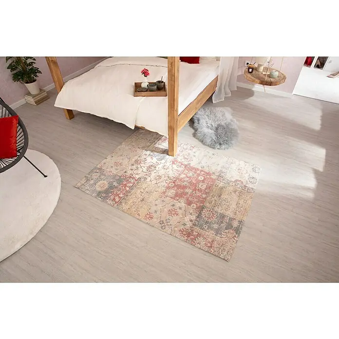 Kayoom Kurzflorteppich IndianaMulti, 170 x 120 cm, 100 % Baumwolle - Ein rechteckiger Teppich mit orientalischem Muster in Rot-, Grau- und Beigetönen liegt unter einem Himmelbett auf einem hellen Holzboden.