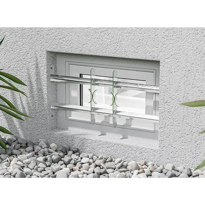 Stabilit Fenstergitter - Höhe: 300 mm, Auszugslänge: 50 cm - 65 cm, Fensterlaibungsmontage - Nahaufnahme eines Kellerfensters mit Sicherheitsgitter, umgeben von Kies und Pflanze.