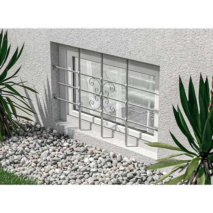 Fenstergitter Milo - B x H: 120 x 69 cm, Montage Fenstergitter: Fensterlaibungsmontage - Nahaufnahme eines Fensters mit stilvollem Fenstergitter, eingebettet in eine Wand mit Pflanzen und Kiesbett.