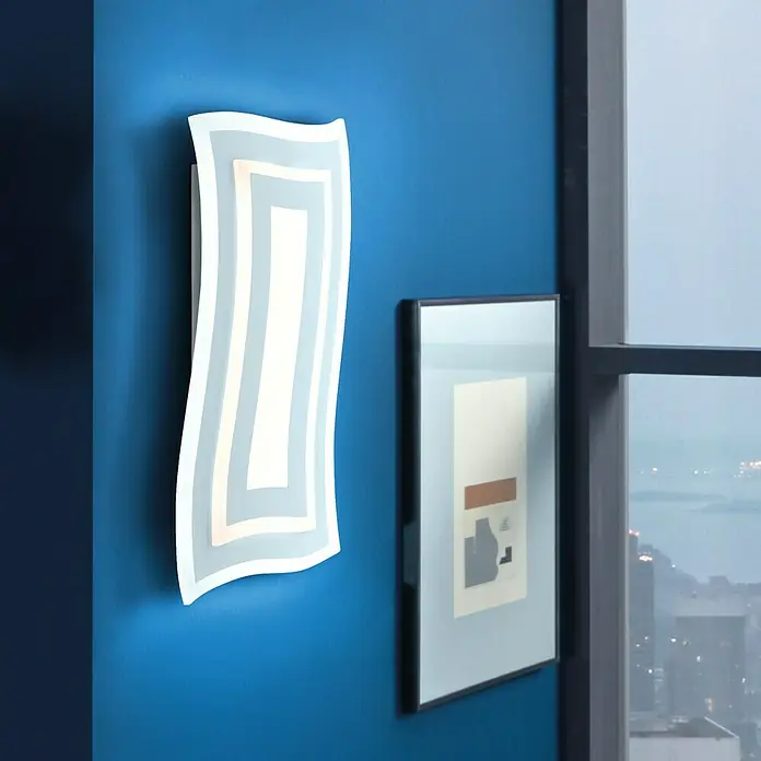 Fischer & Honsel LED-Wandleuchte Gorden - 19 W, L x B x H: 5,5 x 22 x 43 cm, Weiß, Mehrfarbig - Ein modernes, wellenförmiges LED-Wandlicht in einem blauen Raum, das neben einem gerahmten Kunstwerk hängt und eine stimmungsvolle Beleuchtung erzeugt.