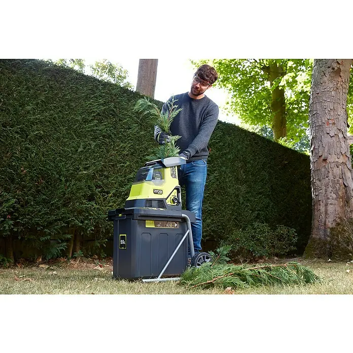 Ryobi Max Power Akku-Häcksler RY36SHX40-0 - Max. Aststärke: 4 cm - Ein Mann benutzt einen Ryobi Häcksler im Garten. Das Gerät ist gelb und schwarz und zerkleinert Äste.
