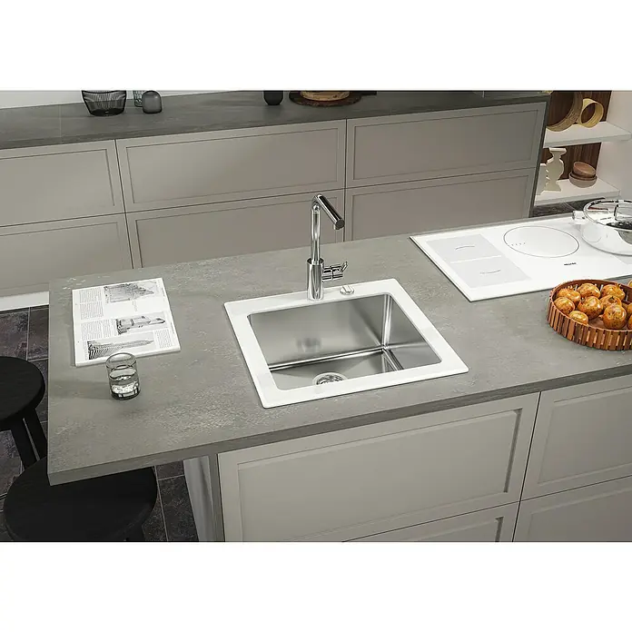 Respekta Einbauspüle New York - 55 x 53 cm, Edelstahl, Weiß - Eine Küchenspüle aus Edelstahl mit einem modernen Wasserhahn auf einer grauen Arbeitsplatte mit Kochfeld und Utensilien.