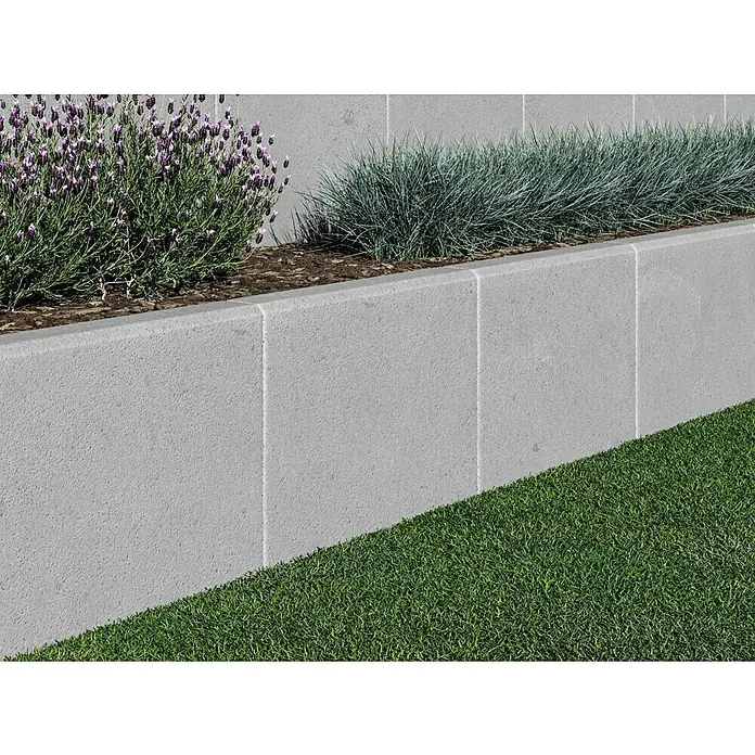 Diephaus L-Stein - 30 cm, 40 cm, Stärke: 7 cm, Grau - Nahaufnahme einer grauen Betonstützmauer mit Pflanzen oben und Rasen unten, die die Vielseitigkeit und Haltbarkeit von Betonprodukten hervorhebt.