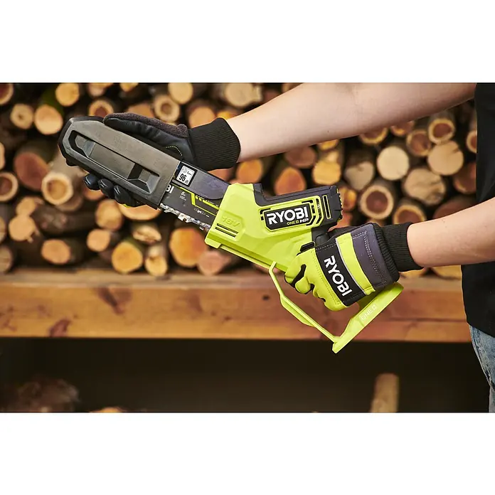 Ryobi ONE+HP Akku-Astsäge RY18PSX15A-0 - 18 V, Li-Ionen, Ohne Akku, Schwertlänge: 15 cm - Nahaufnahme einer Person, die eine Ryobi Akku-Kettensäge vor einem Holzstapel hält.