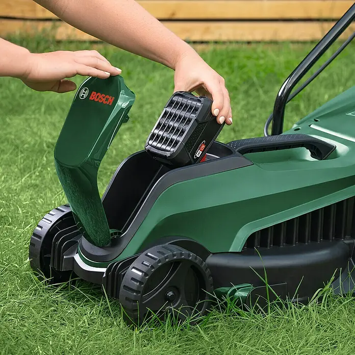 Bosch Power for All 18V Akku-Rasenmäher EasyMower 18V-32-150 - 18 V, 1 Akku, 3 Ah, Schnittbreite: 32 cm - Eine Person setzt einen Akku in einen grünen Bosch-Rasenmäher ein, um ihn für die Gartenarbeit vorzubereiten.