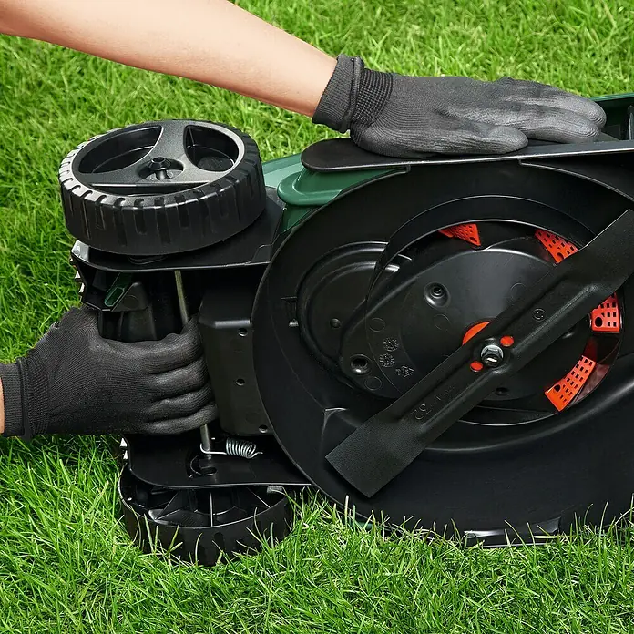 Bosch Power for All 18V Akku-Rasenmäher EasyMower 18V-32-150 - 18 V, 1 Akku, 3 Ah, Schnittbreite: 32 cm - Nahaufnahme eines Rasenmähers auf Gras mit einer Person, die ihn mit Handschuhen wartet oder inspiziert.