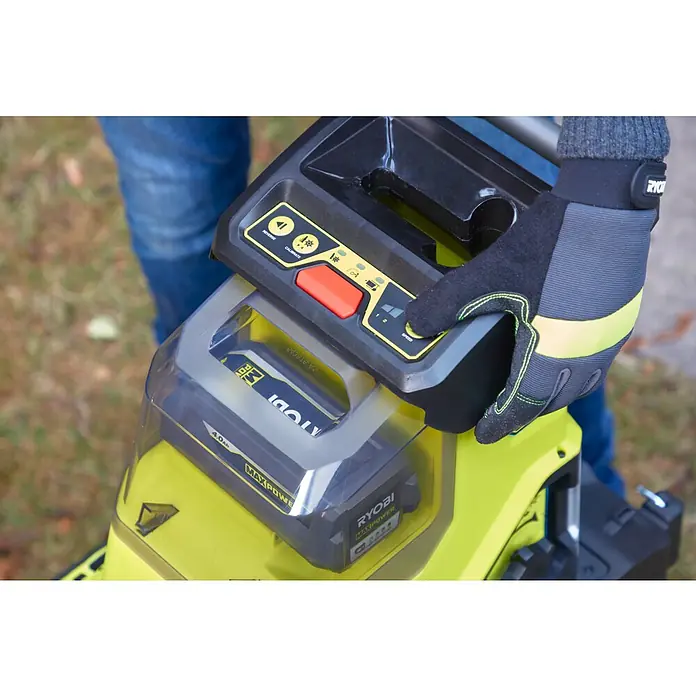 Ryobi Max Power Akku-Häcksler RY36SHX40-0 - Max. Aststärke: 4 cm - Nahaufnahme eines Ryobi-Gartengeräts mit einem Akku und Bedienelementen, das von einer Hand mit Arbeitshandschuh bedient wird.