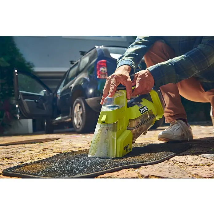 Ryobi ONE+ Akku-Nass-Trockensauger RDC18-0 - 18 V, Ohne Akku, Behältervolumen: 200 l - Ein Mann reinigt eine Fußmatte mit einem gelben Ryobi Swift Clean Teppichreiniger im Freien. Im Hintergrund ist ein Auto zu sehen.