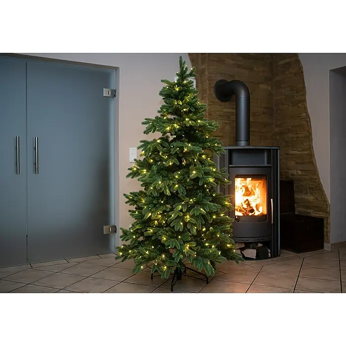 Künstlicher Weihnachtsbaum Roswell - Höhe: 210 cm, Grün, LED-Beleuchtung - Geschmückter Weihnachtsbaum mit warmen Lichtern vor einem Kamin, der eine gemütliche und festliche Atmosphäre schafft. Perfekt für die Feiertage.