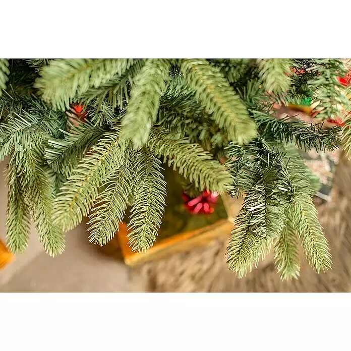 50 NRTH Künstlicher Weihnachtsbaum Vermont - Höhe: 180 cm, Grün, Standfuß - Nahaufnahme von grünen künstlichen Weihnachtsbaumzweigen mit verschwommenen festlichen Dekorationen darunter.