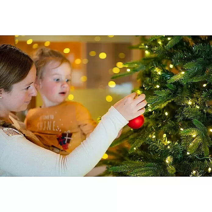 LED-Weihnachtsbaum Richmond - Höhe: 228 cm - Eine Frau und ein Kind schmücken einen Weihnachtsbaum mit einer roten Kugel, ein festlicher Familienmoment.