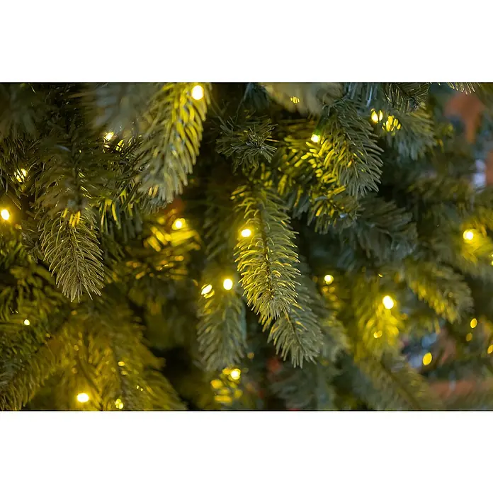 50 NRTH Künstlicher Weihnachtsbaum Vermont - Höhe: 180 cm, Grün, LED-Beleuchtung - Nahaufnahme eines beleuchteten Weihnachtsbaums mit grünen Nadeln und warm leuchtenden Lichtern, die eine festliche Atmosphäre schaffen.