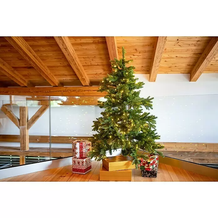 Künstlicher Weihnachtsbaum Roswell - Höhe: 150 cm, Grün, LED-Beleuchtung - Ein grüner künstlicher Weihnachtsbaum mit warmen Lichtern, umgeben von Geschenkboxen auf Holzboden.