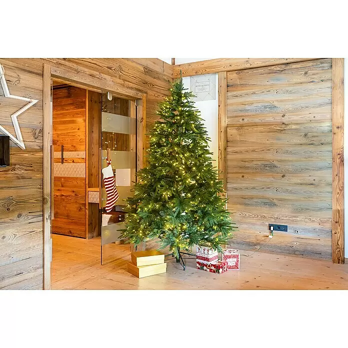 LED-Weihnachtsbaum Richmond - Höhe: 228 cm - Ein künstlicher grüner Weihnachtsbaum mit warmweißen Lichtern und Geschenkkartons darunter, in einem holzvertäfelten Raum.