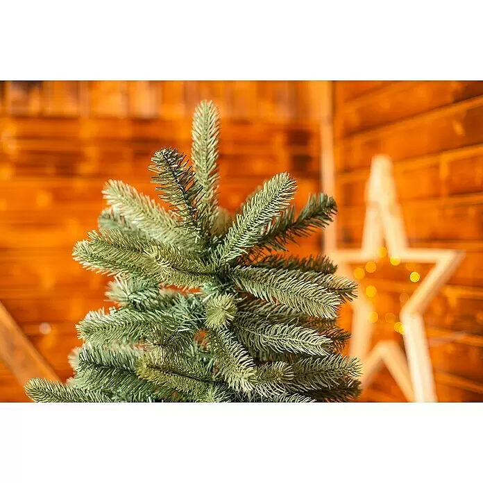 50 NRTH Künstlicher Weihnachtsbaum Vermont - Höhe: 180 cm, Grün, Standfuß - Grüne Kunstweihnachtsbaumzweige vor einem unscharfen warmen Holzhintergrund und leuchtender Sterndekoration.
