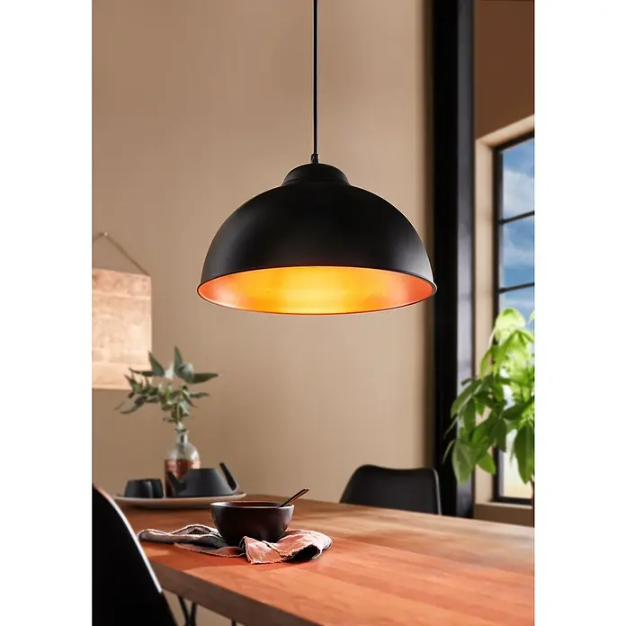 Eglo Pendelleuchte rund - Schwarz/Kupfer - Eine schwarze Hängelampe mit goldfarbenem Innenraum hängt über einem Holztisch und beleuchtet ihn warm. Dekorative und stimmungsvolle Beleuchtung.