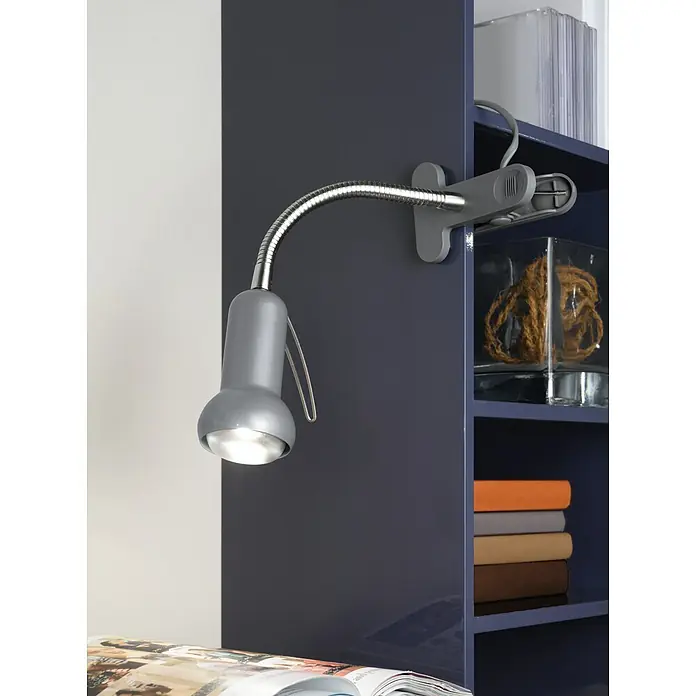 Eglo Klemmleuchte Fabio - 40 W, Farbe Gehäuse: Silber - Nahaufnahme einer silbernen Klemmleuchte mit flexiblem Schwanenhals, die an einem Regal befestigt ist und Licht auf eine Zeitschrift wirft.