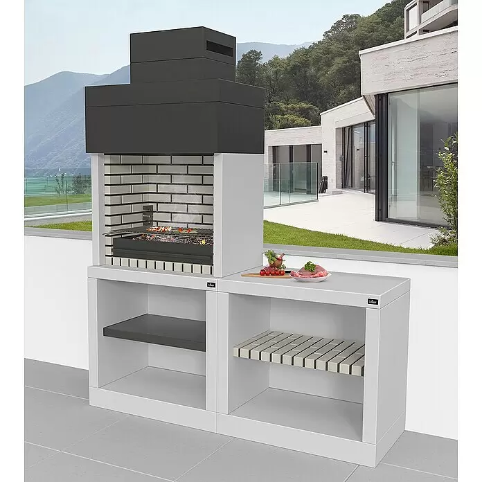 Barbacoa con chimenea Vilamoura con mesa lateral - An x Pr x Al: 180 x 58 x 210 cm, Superficie parrilla: 71,5 x 53 cm, Hormigón, Blanco/Negro - Estación de barbacoa exterior con chimenea oscura, brasero de ladrillo claro y módulos de almacenamiento blancos, lista para asar en un patio.