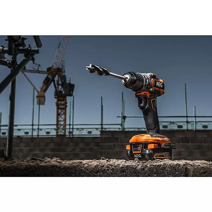 AEG Pro 18V Taladro atornillador de batería BS18SBL-202C - 18 V, 2 baterías, 2 Ah, 60 Nm - Taladro atornillador AEG naranja y negro con una broca grande, sobre suelo áspero en una obra.