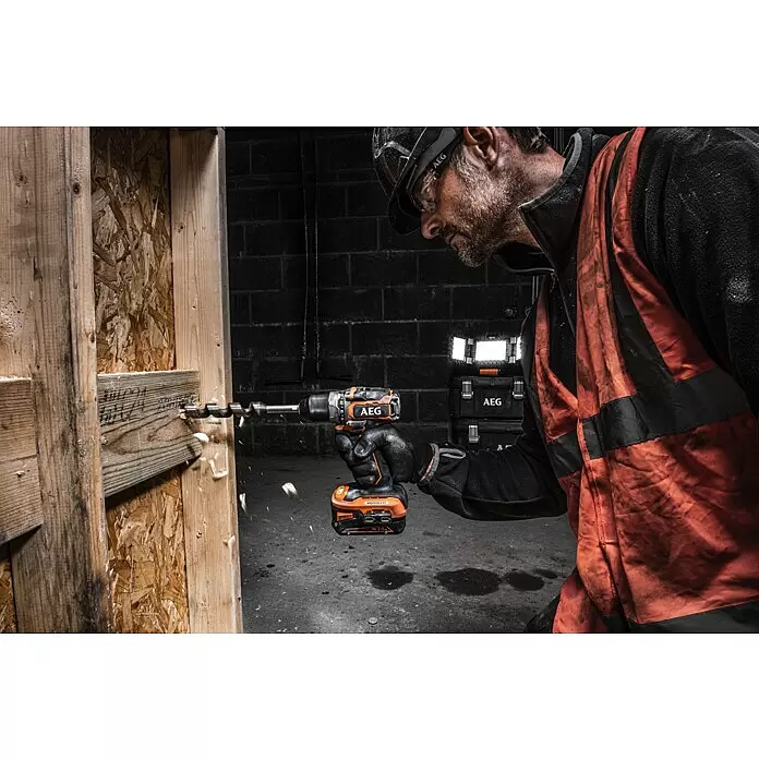 AEG Pro 18V Taladro atornillador de batería BS18SBL-202C - 18 V, 2 baterías, 2 Ah, 60 Nm - Un taladro inalámbrico AEG naranja y negro con broca de barrena, usado por una persona para perforar una viga de madera, creando virutas.