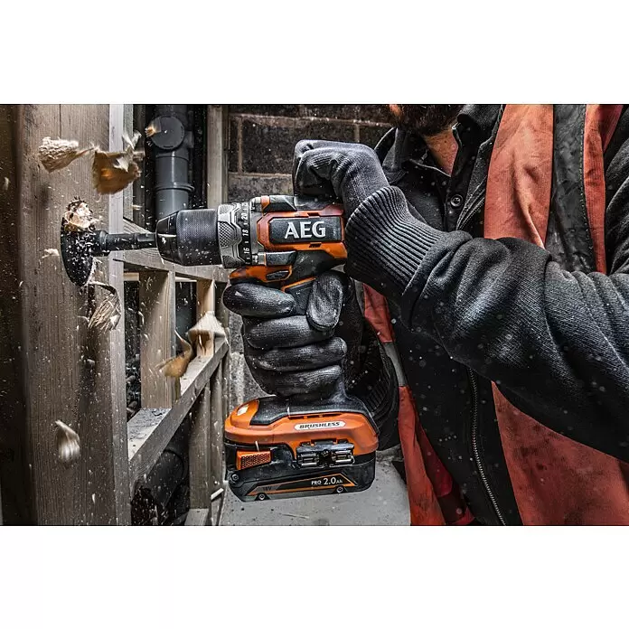 AEG Pro 18V Taladro atornillador de batería BS18SBL-202C - 18 V, 2 baterías, 2 Ah, 60 Nm - Taladro inalámbrico AEG naranja y negro con sierra de corona, perforando madera y creando virutas voladoras. Una mano enguantada lo sujeta.