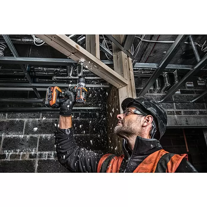 AEG Pro 18V Taladro atornillador de batería BS18SBL-202C - 18 V, 2 baterías, 2 Ah, 60 Nm - Hombre usa un taladro AEG naranja y negro para perforar una viga de madera, con virutas volando.