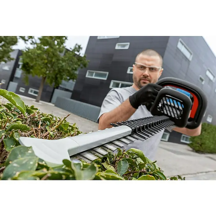 Bosch Professional AMPShare 18V Akku-Heckenschere GHE 18V-50 - 18 V, Ohne Akku, Schnittlänge: 50 cm - Nahaufnahme einer Heckenschere in Aktion, bedient von einem Mann mit Schutzbrille und Handschuhen, vor einem modernen Gebäude.