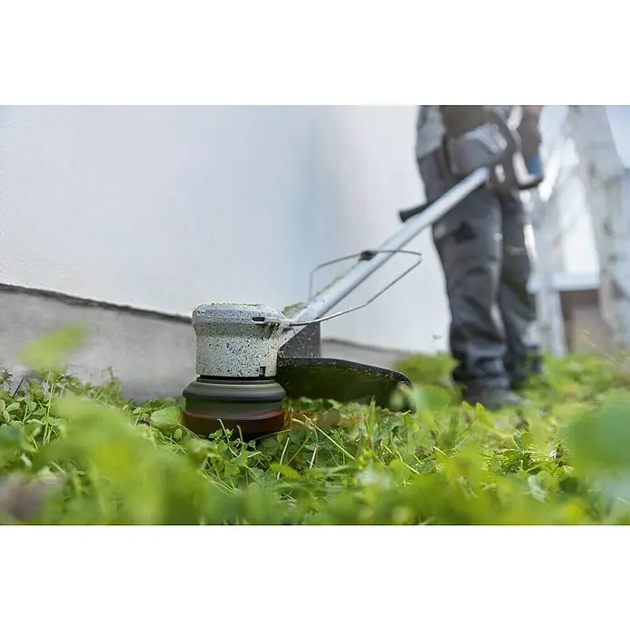 Bosch Professional AMPShare 18V Akku-Rasentrimmer GRT 18V-33 - 18 V, Ohne Akku - Nahaufnahme eines Rasentrimmers, der von einer Person bedient wird, um das Gras an der Wand zu schneiden, wobei der Trimmer im Fokus steht.
