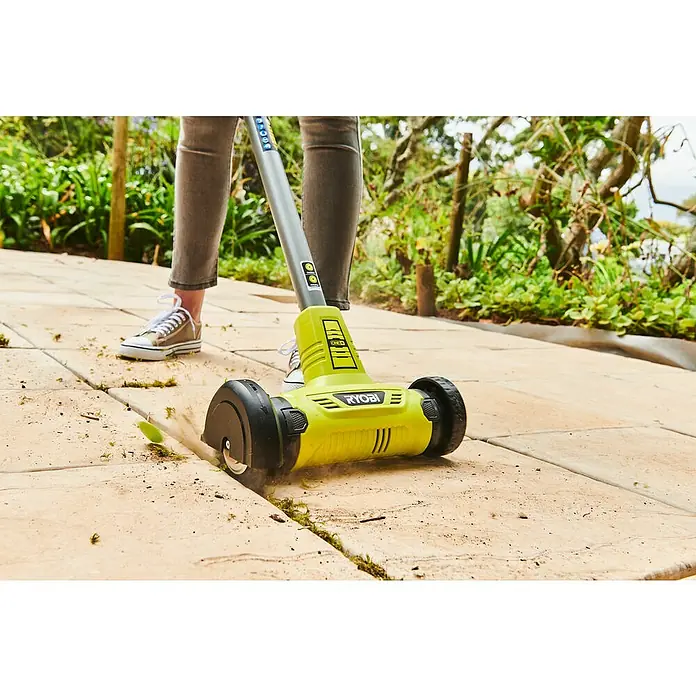Ryobi Ersatzbürste RAC818 - Grau, Passend für: Fugenreiniger RY18PCA - Eine Person verwendet einen Ryobi Kantenschneider, um Gras zwischen Pflastersteinen zu entfernen. Der Kantenschneider ist gelb mit schwarzen Rädern.
