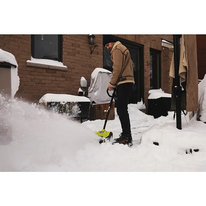 Ryobi ONE+ Akku-Schneefräse RY18ST25A-0 - 18 V, Ohne Akku, Arbeitsbreite: 25 cm - Ein Mann benutzt einen gelben Ryobi Schneefräse, um Schnee von einem Backsteinhof zu räumen.